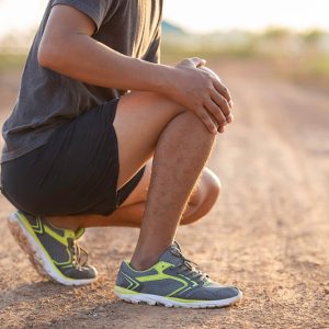 Knee injury concept from exercise : Asian man hands on knee while running on park road. Shot in the morning, sunlight and warm effects.