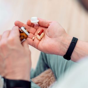 Cropped photo of unrecognized person shaking a glass bottle and putting pills into his hand